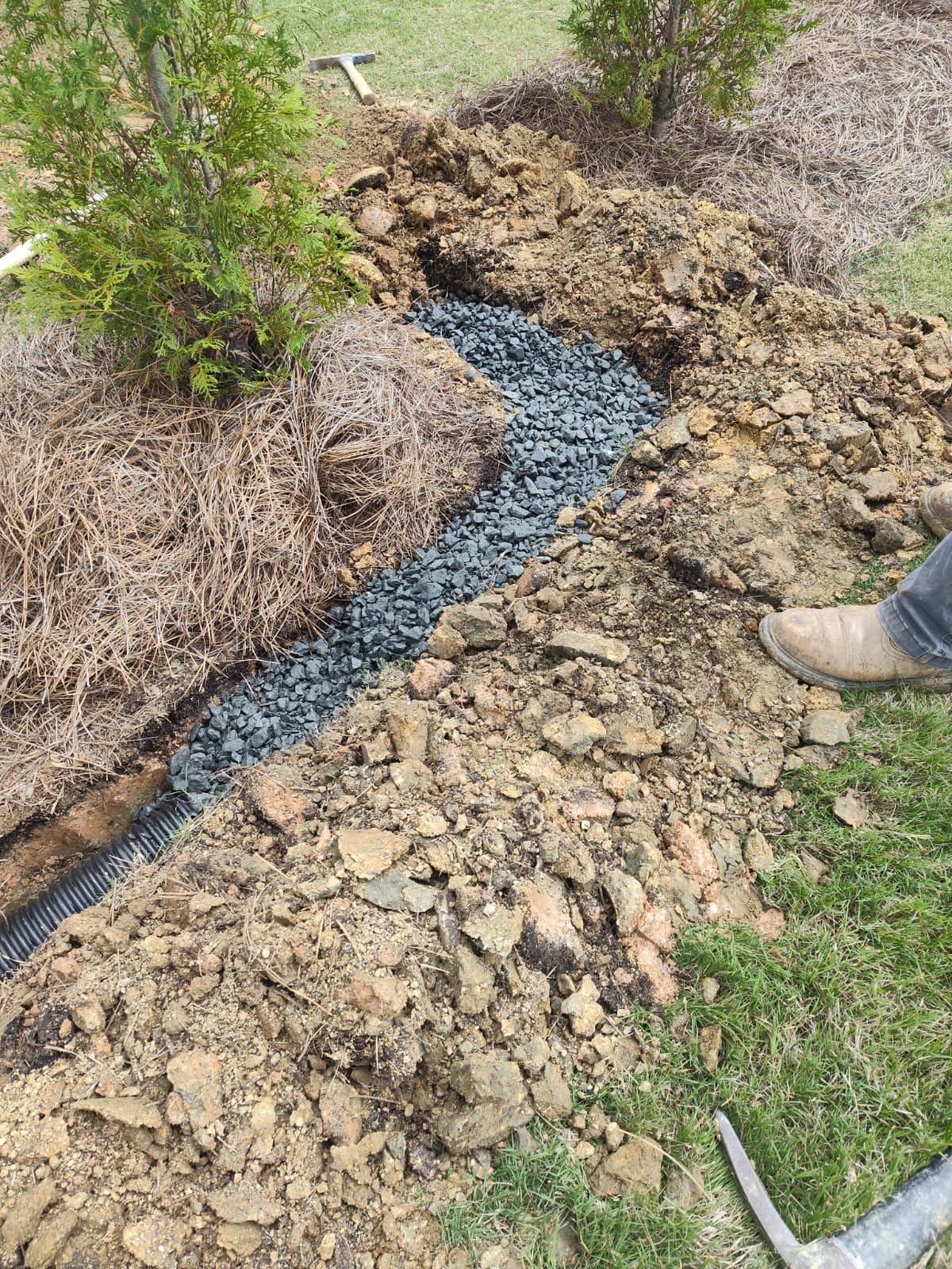 Professional drainage trench with gravel and perforated pipe in a landscaped yard