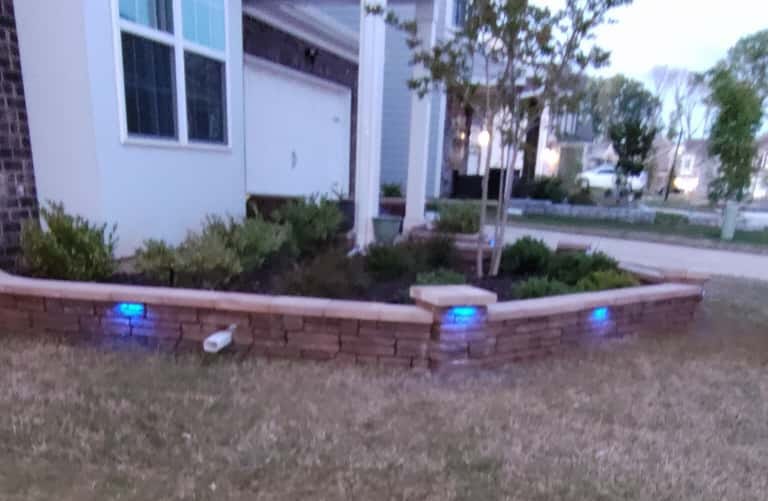 Front yard paver planter wall with integrated LED accent lights illuminated at dusk